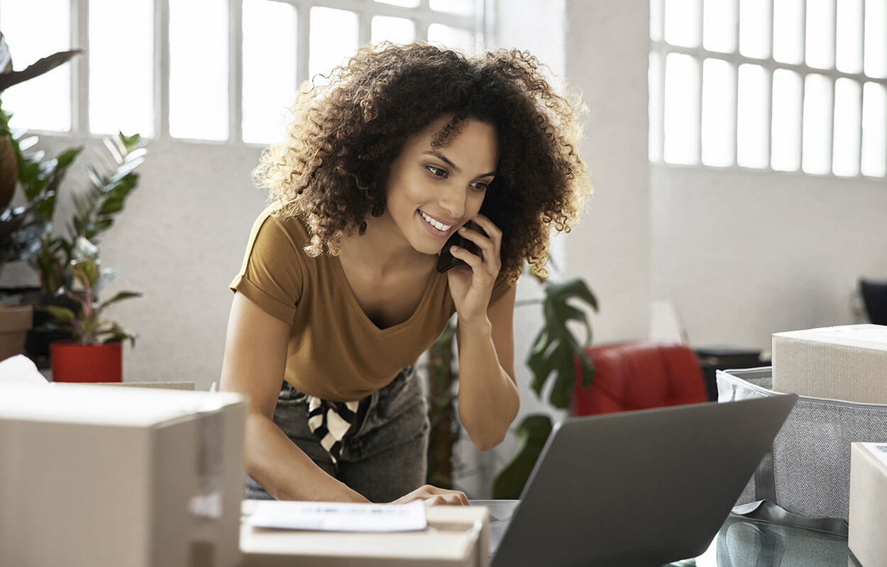 Woman on her mobile while standing at her desk working on a laptop